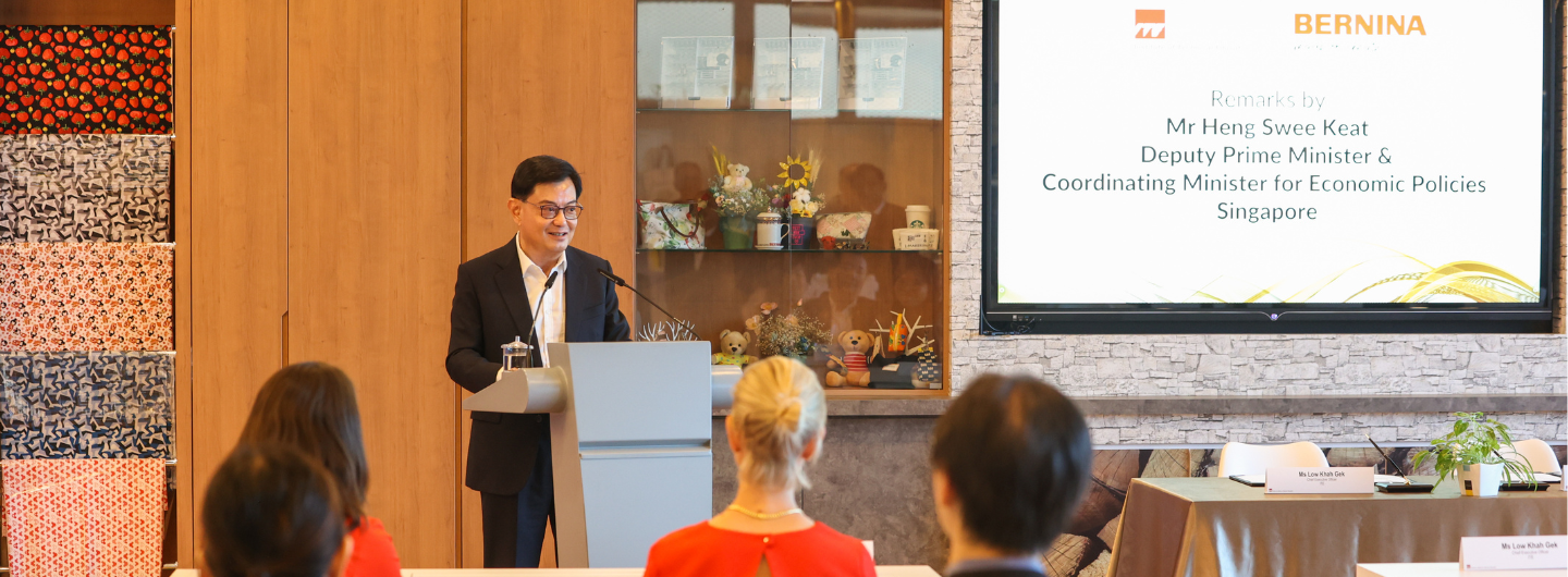 Man at lectern with Bernina logo on screen stating Heng Swee Keat's title, audience present.